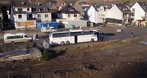 Landschaftsaufnahme eines Dorfs, ein großer Reisebus steht auf einer matschigen Straße