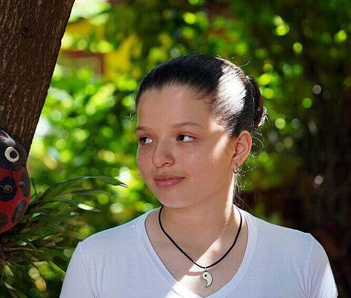 Luz tritt selbstbewusst an das Thema Menstruation heran Ein Mädchen mit weißem Shirt steht vor einem Baum im Schatten und blickt zur Seite