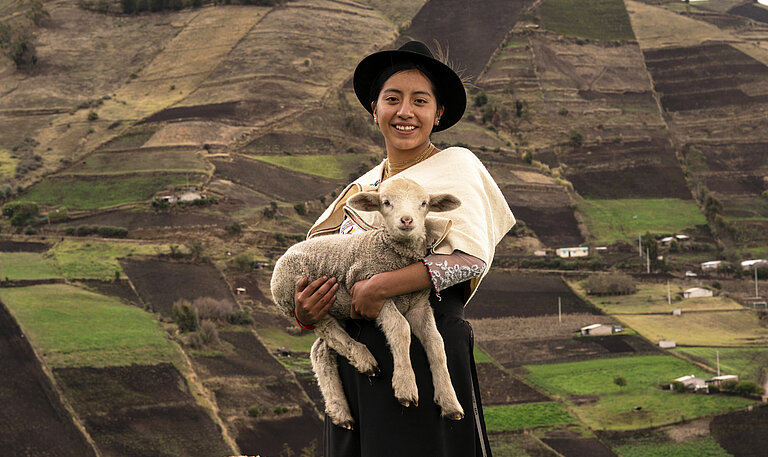 Junge Frau in hügeliger Landschaft mit Lamm auf dem Arm