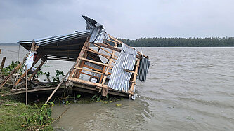Die Überreste eines Hauses werden von einer Überschwemmung langsam in den Fluss gezogen.