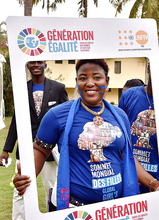 SDG-Event Eine junge Frau, die zwei blaue Striche auf der Wange hat, hält einen großen Rahmen hoch und schaut hindurch