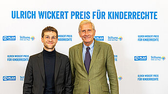 Anton Stanislawski steht neben Ullrich Wickert vor einem Hintergrund, auf dem "Ulrich Wickert Preis für Kinderrechte" steht
