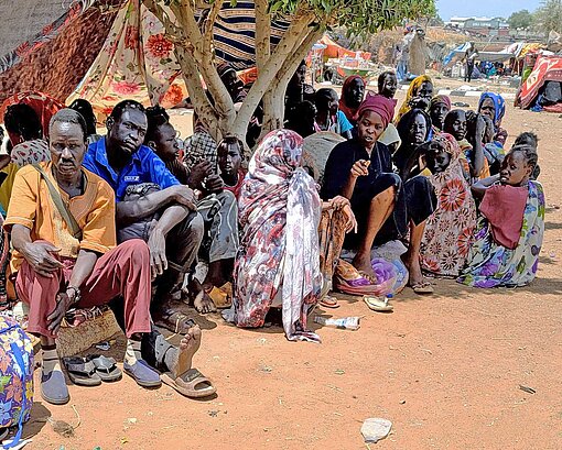 Erschöpft und müde erreichen geflüchtete Familien aus Sudan das Nachbarland Südsudan Kinder, Frauen und Männer sitzen unter einer Zeltplane