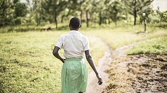 Ein Mädchen von hinten, dass draußen über einen unbefestigten Weg läuft