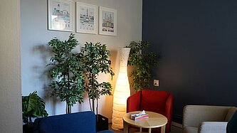 In einem Therapieraum stehen drei Sessel um einen kleinen Tisch herum. Daneben stehen einige Pflanzen und eine Papierlampe sorgt für gemütliches Licht.