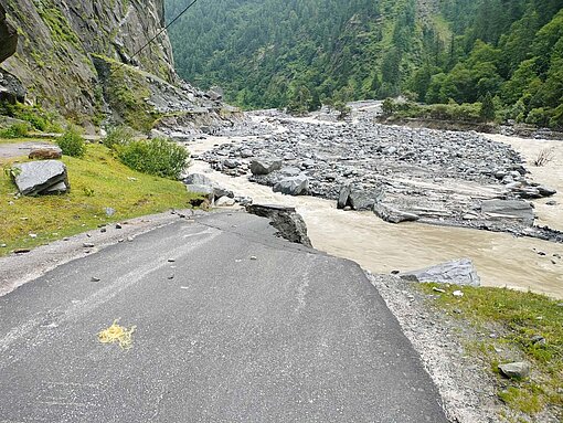 Eine Straße in einem begrünten Tal ist von einem reißenden Fluss weggerissen worden