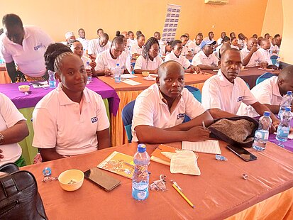 Männer und Frauen sitzen in einem Kursraum an Tischen