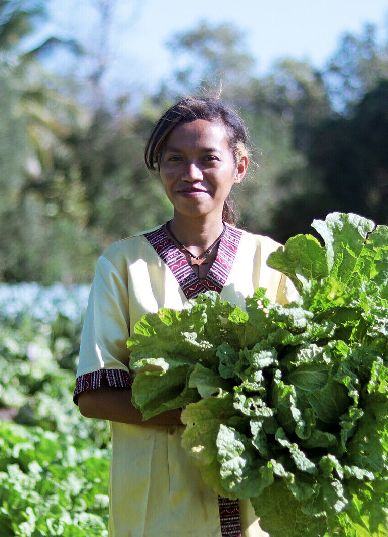 Eine junge Frau steht auf einem Feld und hält einen großen Kohl in der Hand