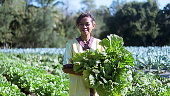 Eine junge Frau steht auf einem Feld und hält einen großen Kohl in der Hand