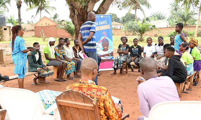 Junge Menschen mit Lehrenden sitzen draußen im Kreis und nehmen an einer Schulung teil