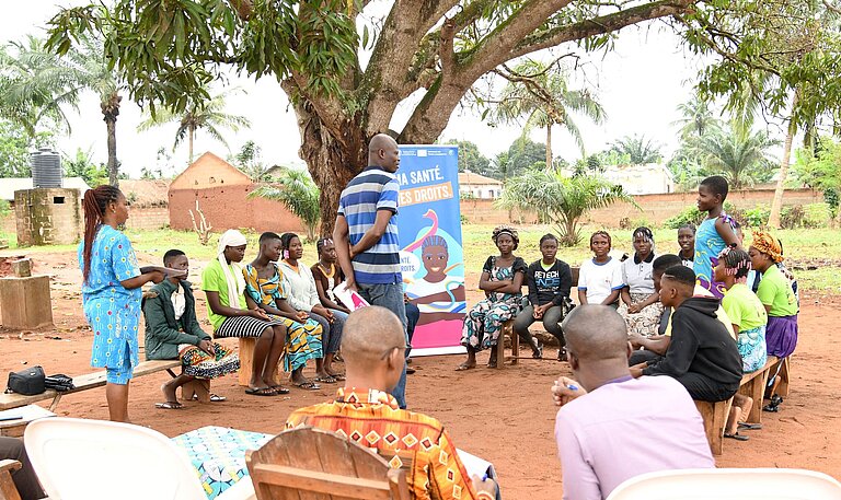 Junge Menschen mit Lehrenden sitzen draußen im Kreis und nehmen an einer Schulung teil
