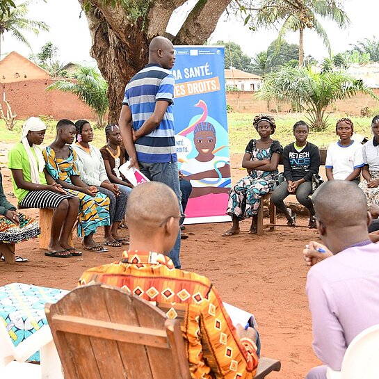 Junge Menschen mit Lehrenden sitzen draußen im Kreis und nehmen an einer Schulung teil
