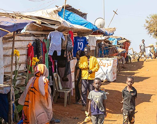 Vor Hütten aus Stroh und Blech laufen Personen