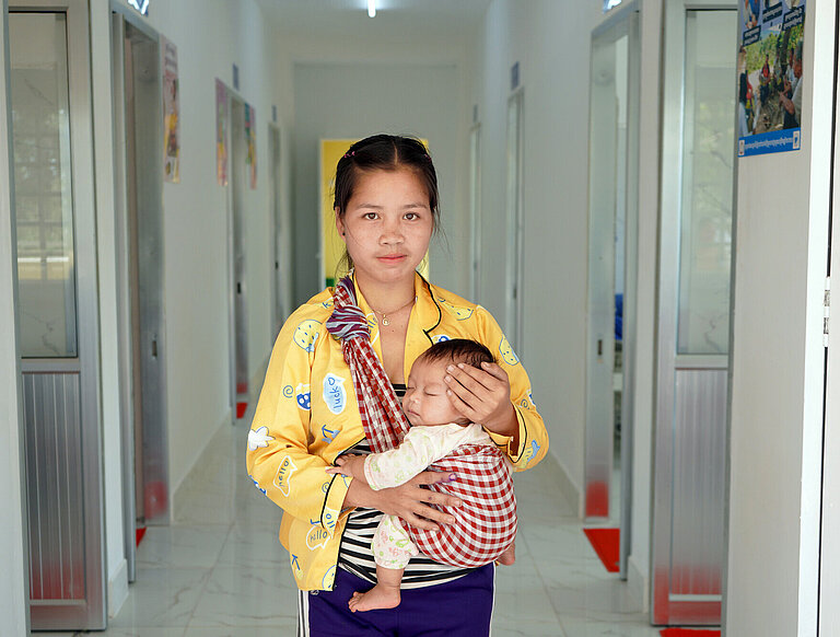 Eine Mutter steht mit ihrem Kind auf dem Arm im Flur des Krankenhauses