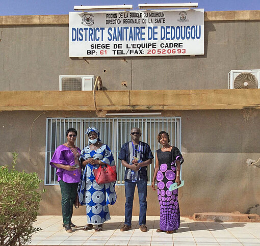 Die Fachleute im Plan-Projekt kooperieren mit medizinischen Zentren und Gesundheitsstationen in Burkina Faso Vier Personen stehen vor einem Gebäude
