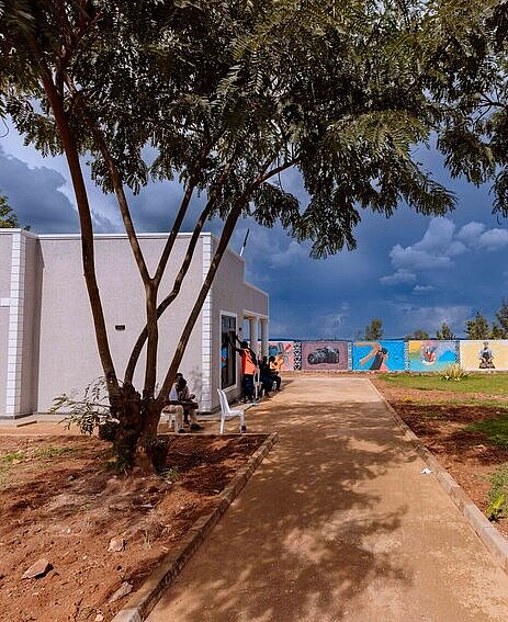 Graues Gebäude mit einem begrünten Platz davor, umgeben von einer bunt bemalten Mauer