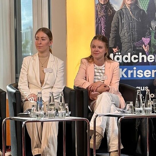 vier junge Frauen sitzen auf einer kleinen Bühne nebeneinander in Sesseln