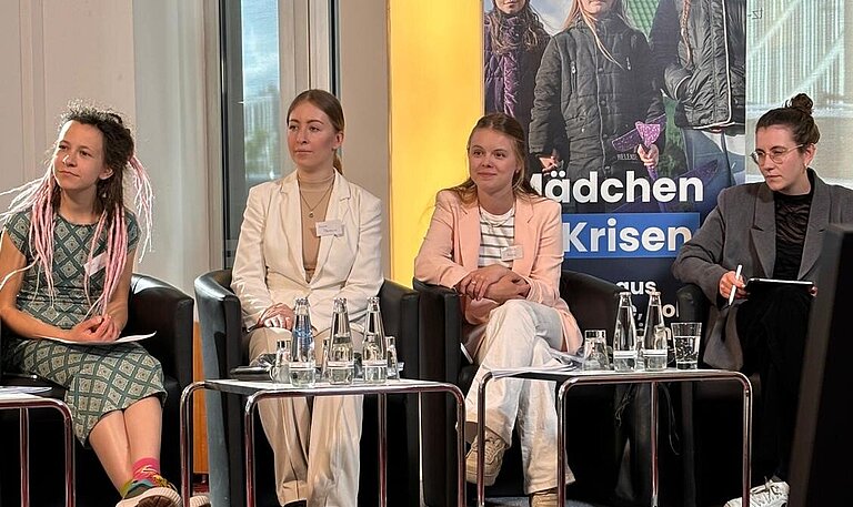 vier junge Frauen sitzen auf einer kleinen Bühne nebeneinander in Sesseln