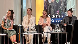 vier junge Frauen sitzen auf einer kleinen Bühne nebeneinander in Sesseln