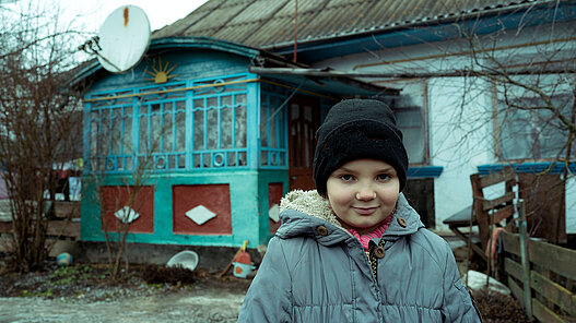 Junges Mädchen in Winterbekleidung steht vor einem Haus in der Ukraine
