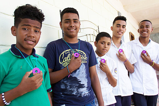 Kolumbianische Jungs lernen mehr über die Menstruation Fünf Jungen haben einen Menstruationstracker um den Hals hängen und halten ihn jeweils mit einer Hand fest