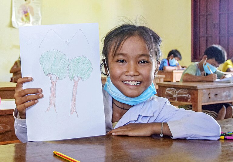 Ein Mädchen zeigt eine Zeichnung von Bäumen