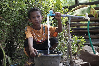 Ein Junge füllt einen Eimer an einer Wasserstation