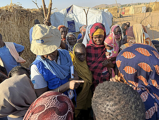 Eine Plan-Mitarbeiterin ist umringt von sudanesischen Frauen und Kindern und spricht mit ihnen