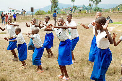 In Ruanda führt eine Gruppe von Mädchen verschiedenen Alters einen Tanz auf. Sie tragen alle die gleiche Kleidung und lachen.