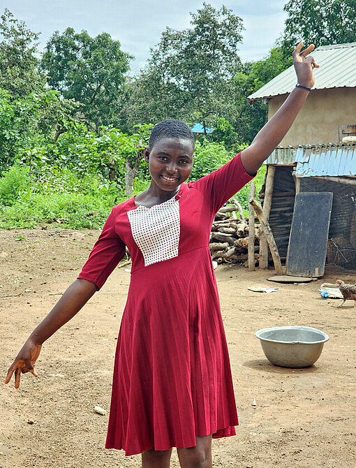 Ein Mädchen in rotem Kleid winkt in die Kamera