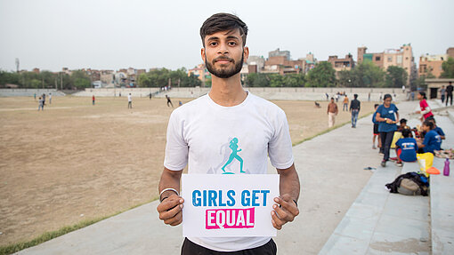 Kushal leitet ein gemischtes Touch-Rugby-Team in Delhi und macht sich für die Sicherheit von Mädchen stark. Kushal auf einem Sportplatz hält ein Girls Get Equal Schild.