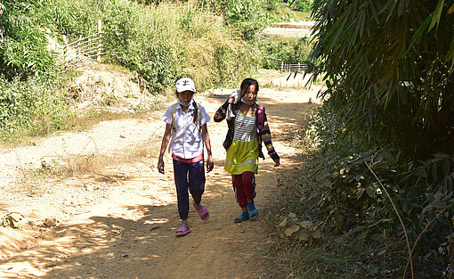 Zwei Schulkinder auf einem Schotterweg.
