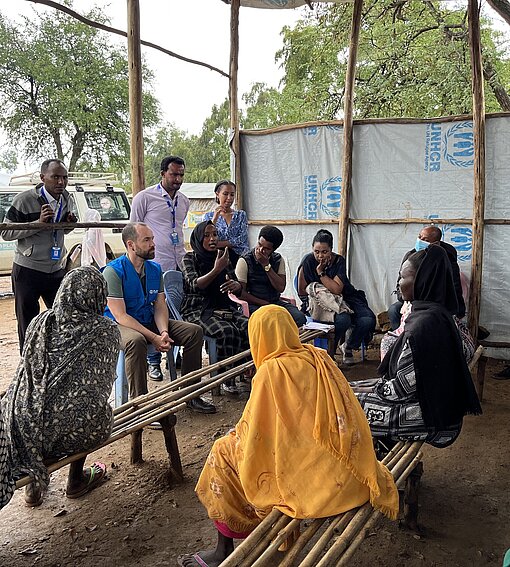 Mehrere Frauen sitzen auf provisorischen Bänken und sprechen mit Mitarbeitern einer Hilfsorganisation