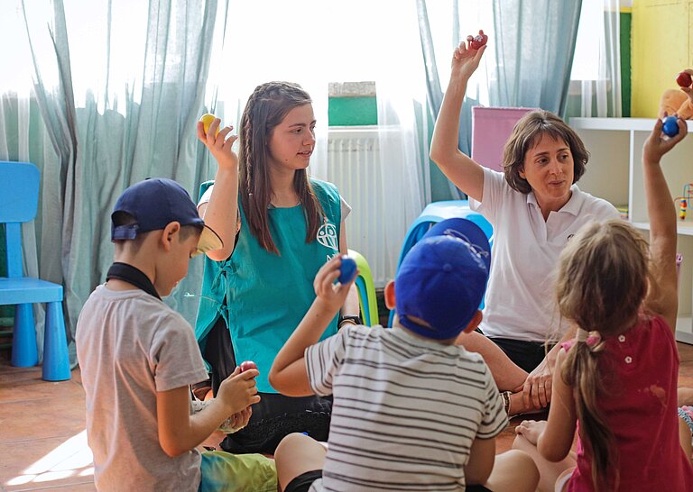 Zwei Erzieherinnen sitzen und spielen mit ukrainischen Kindern in einem Kinderschutzraum