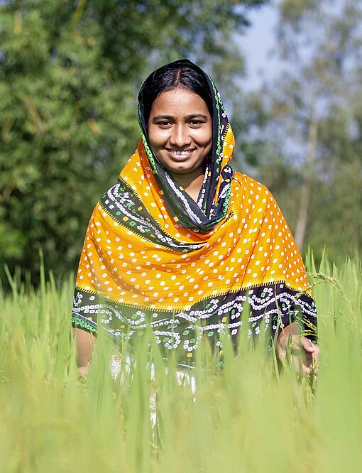 Ein Mädchen mit gelb-buntem Schal läuft lächelnd durch ein Reisfeld
