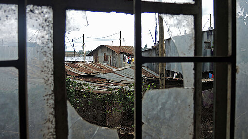Blick aus einem zerbrochenen Fenster auf Häuserdächer.