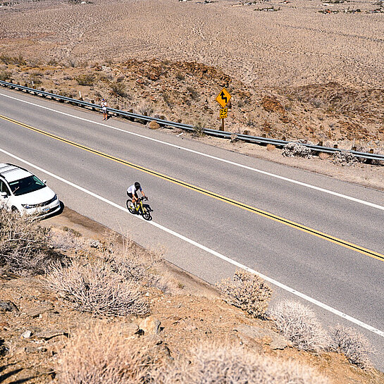 eine lange, leere Straße von oben, auf der ein Rennradfahrer fährt
