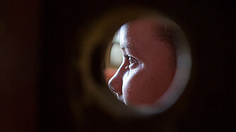 ein Loch in einer Wand, dahinter ist ein Gesicht zu erkennen