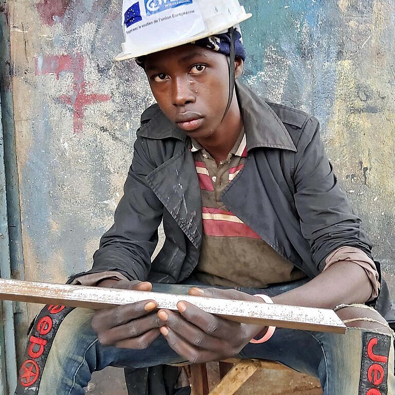 Ein junger Mann sitzt vor einer Werkstatt in Guinea