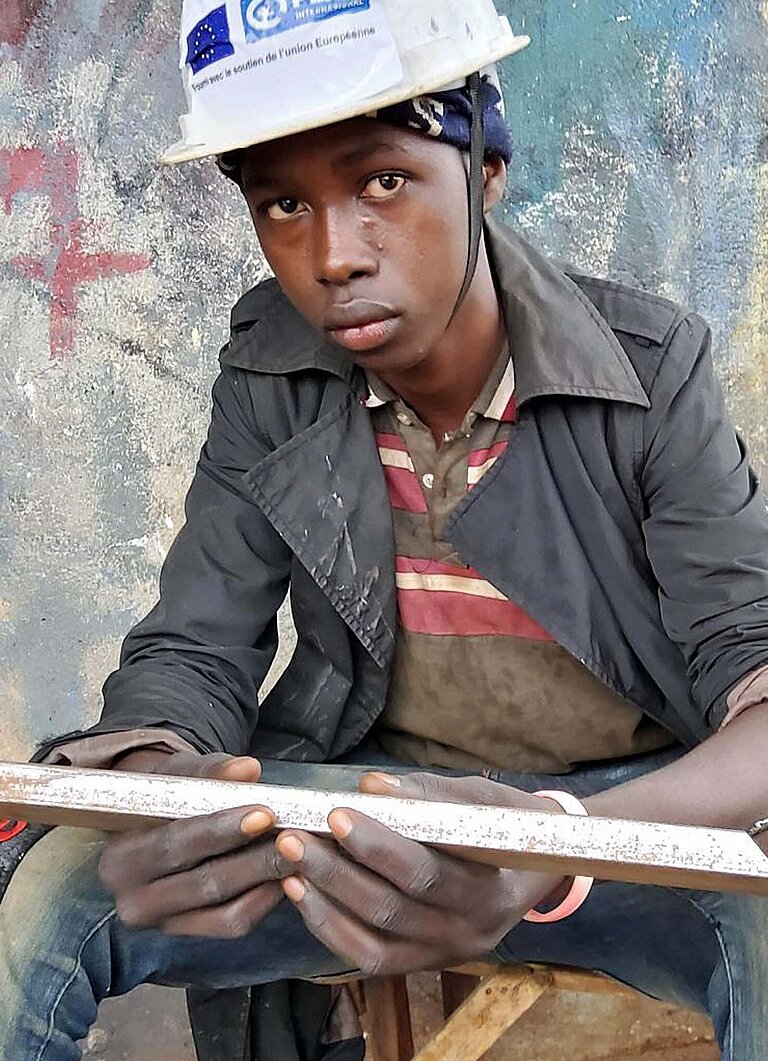 Ein junger Mann sitzt vor einer Werkstatt in Guinea