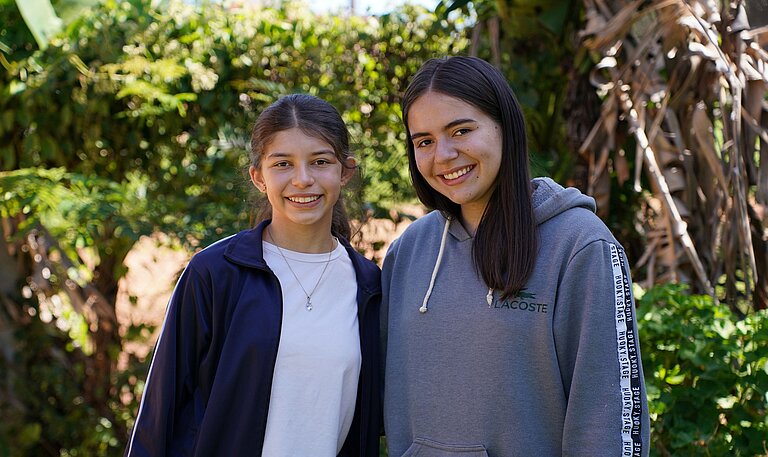 Zwei Mädchen im Teenageralter stehen Schulter an Schulter und lächeln.