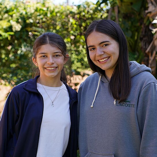 Zwei Mädchen im Teenageralter stehen Schulter an Schulter und lächeln.