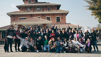 Eine diverse Gruppe Jugendlicher und Erwachsener steht für ein Gruppenfoto zusammen. Sie wirken ausgelassen und fröhlich.