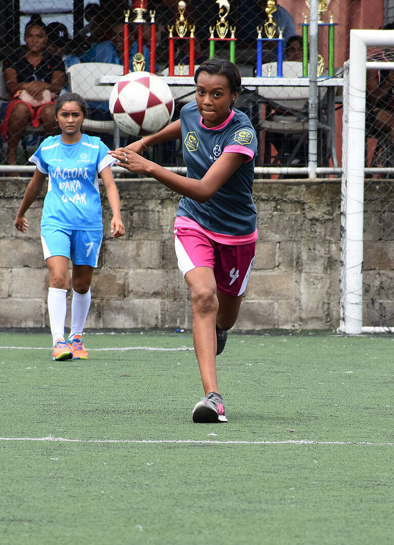 Eine junge Frau auf dem Fußballfeld nimmt konzentriert Anlauf, um einen Ball zu schießen.