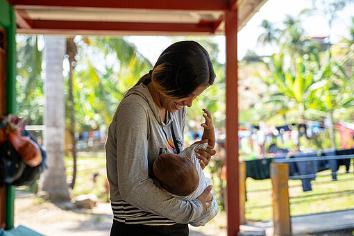 Eine junge Frau hält ein Baby im Arm, sie schaut auf es herab und lacht