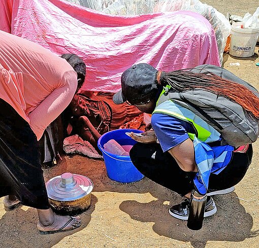 Nothelferinnen befragen geflüchtete Menschen in Südsudan nach ihren Bedürfnissen Zwei Frauen beugen sich zu einer Zeltbewohnerin
