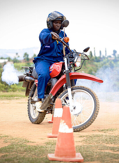 Clarisse fährt draußen in Ruanda ein rotes Motorrad 