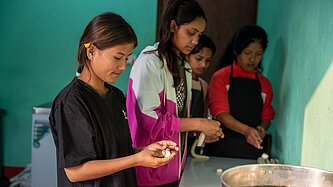 Junge Frauen stehen um einen Tisch und kochen.