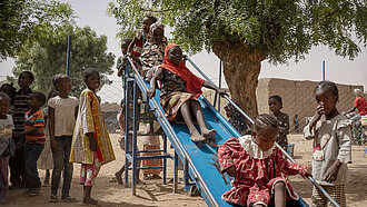 Eine Gruppe Kinder auf einem Spielplatz. Sie stehen an einer Rutsche Schlange und rutschen.