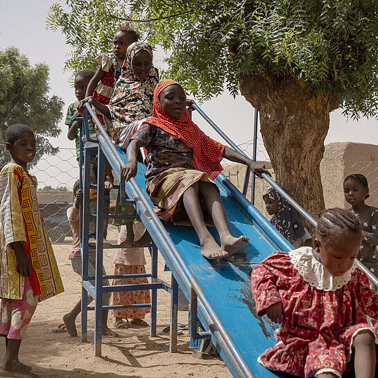 Eine Gruppe Kinder auf einem Spielplatz. Sie stehen an einer Rutsche Schlange und rutschen.